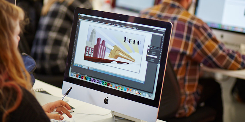 A student working on graphic design software on a desktop.