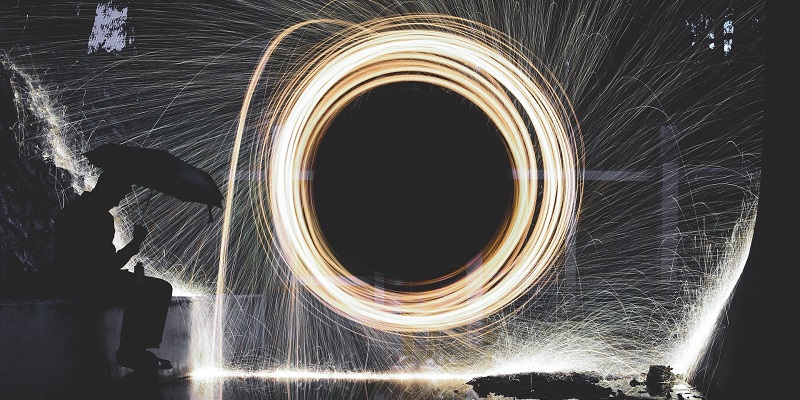 Man in silhouette with umbrella sits by a live Catherine Wheel