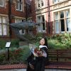 Student posing on a bench in her graduation robe holding a bunch of flowers