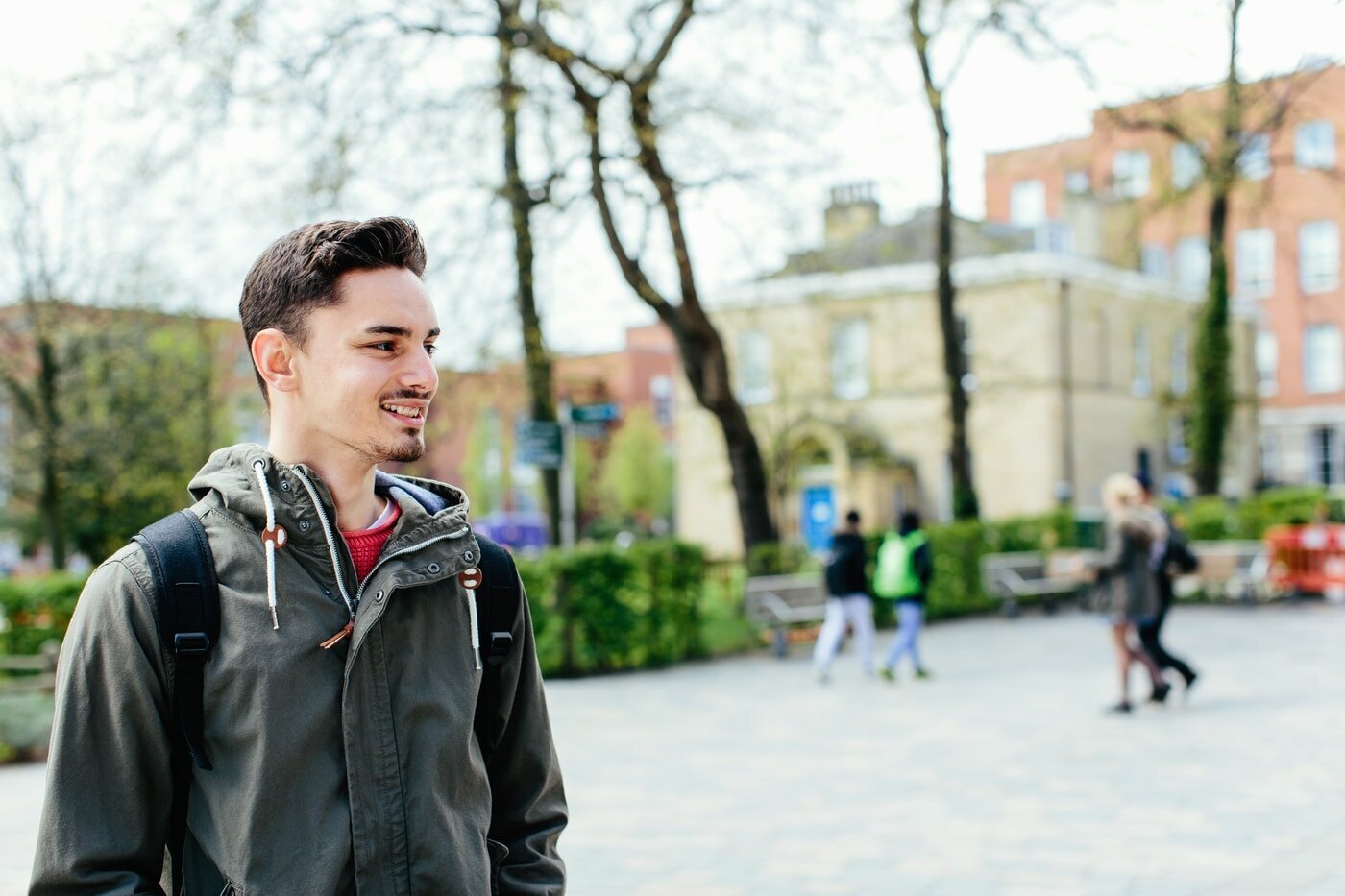 Student stood outside wearing a green coat looking away from the camera and into the distance.