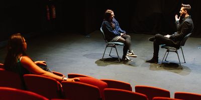 Two people rehearsing a scene while being watched from the audience by another person