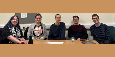 Two women and three men seated round a table smiling at the camera