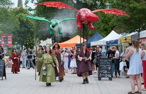 Reenactors holding red and green dragon puppets breathing smoke through a market