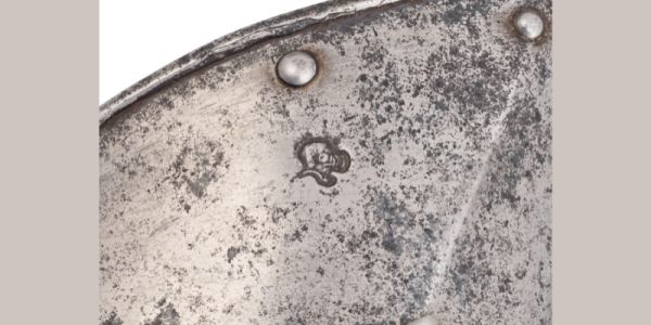 Close up of part of a piece of medieval leg armour, showing a mark stamped into the metal.