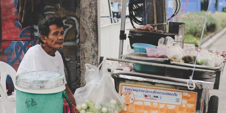 Elderly Thai male street vendor sitting at cart