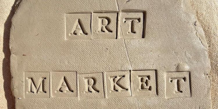 Letters spelling ART MARKET pressed into clay on a canvas background