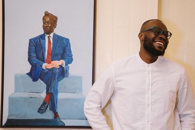 The artist Tonye Ekine standing to the right of one of his paintings