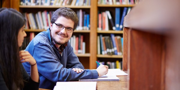 Students sitting at a library desk with bookshelves in background