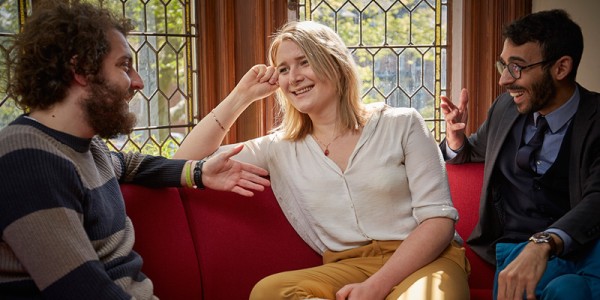 Three students chatting on a sofa in front of window