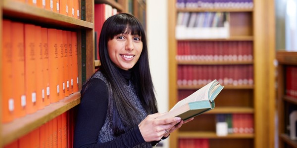 Student reading a book, leaning against shelves of books