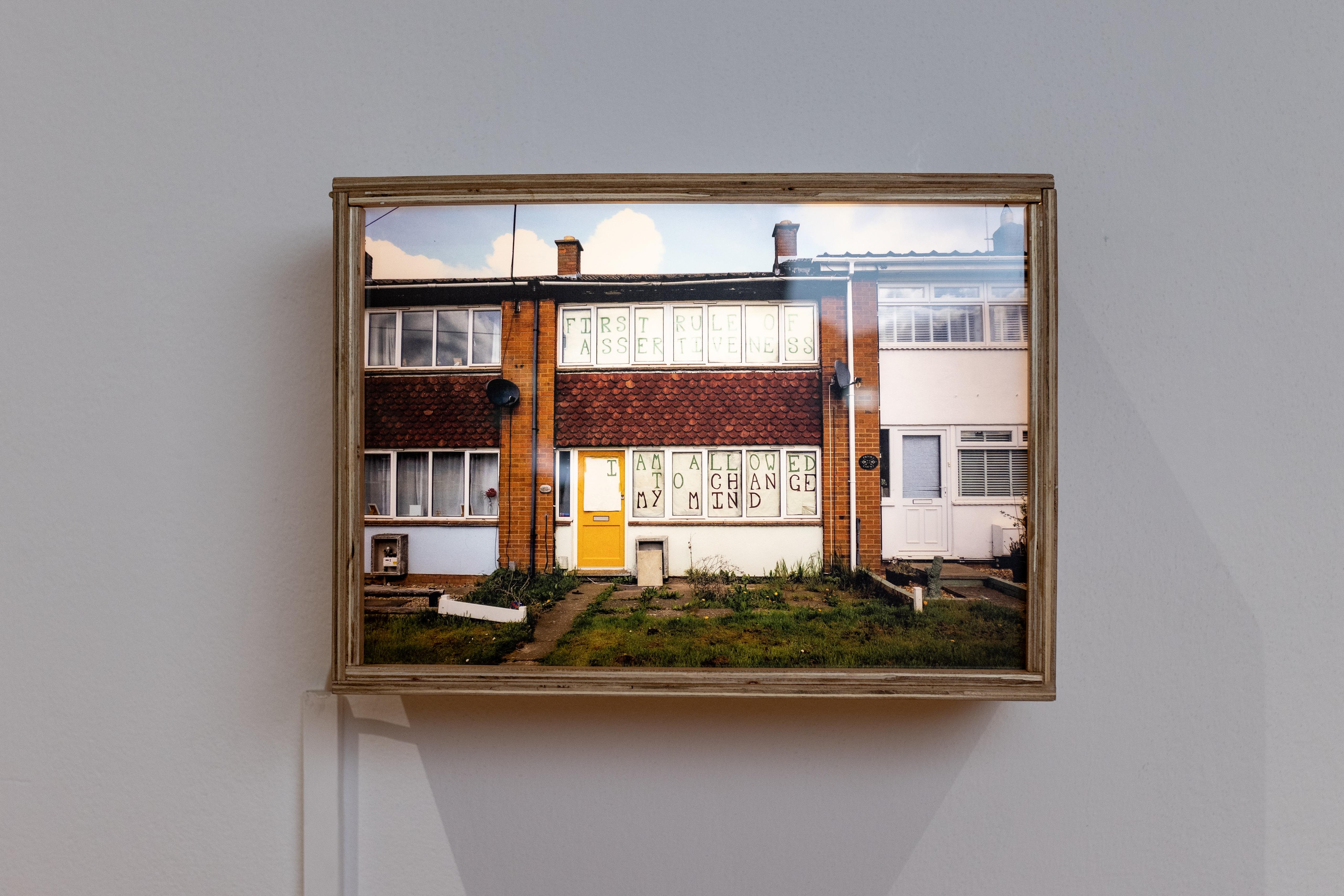 Work by FAHACS student George Storm Fletcher in Leeds Art Gallery. The work is an illuminated photographic print in a wooden frame lightbox and depicts a house with text art in the window.