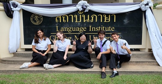 a group of people sitting on a lawn in front of a sign at a Thai university