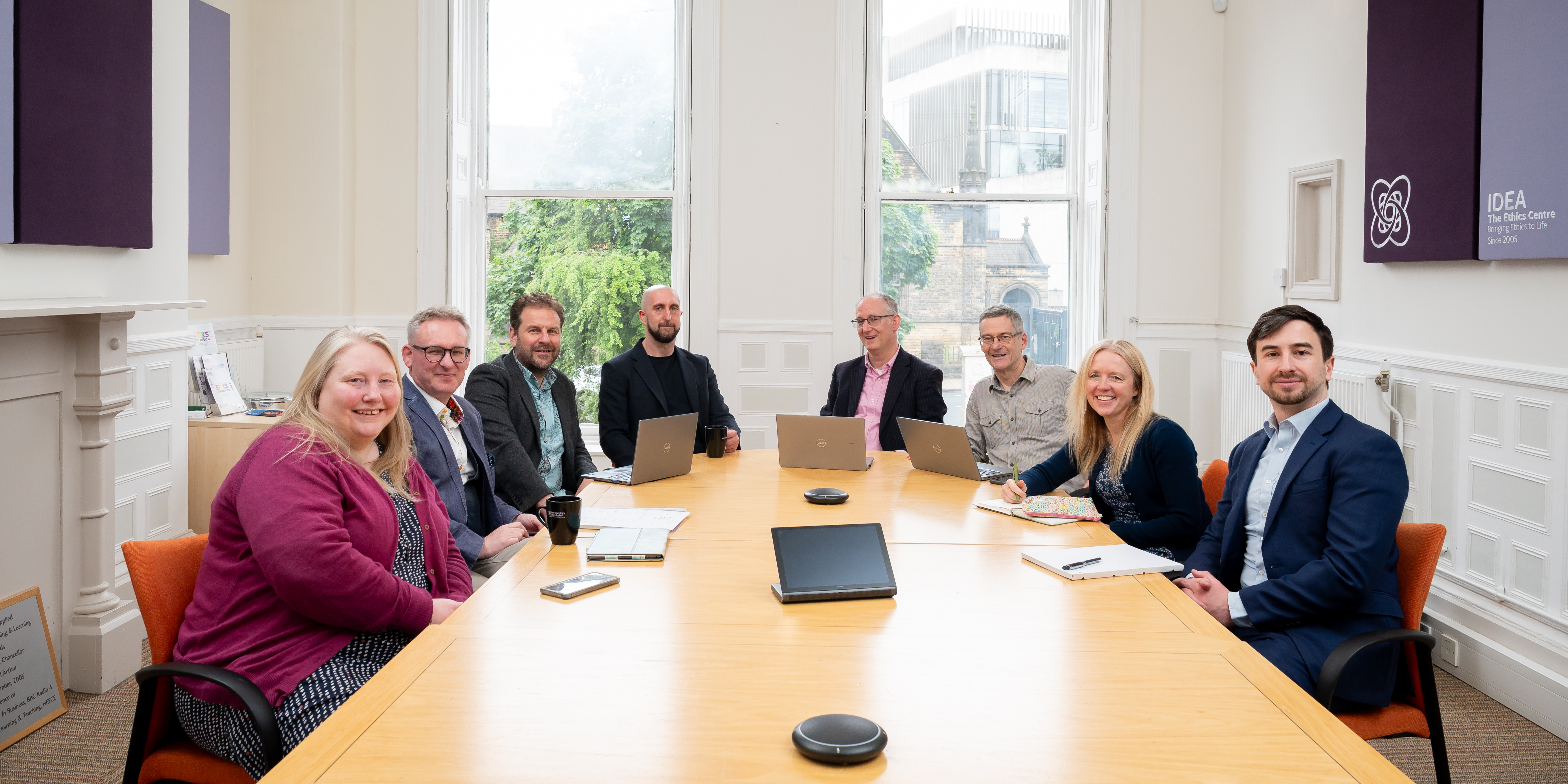 A group of people sitting around a board room table, smiling for the camera