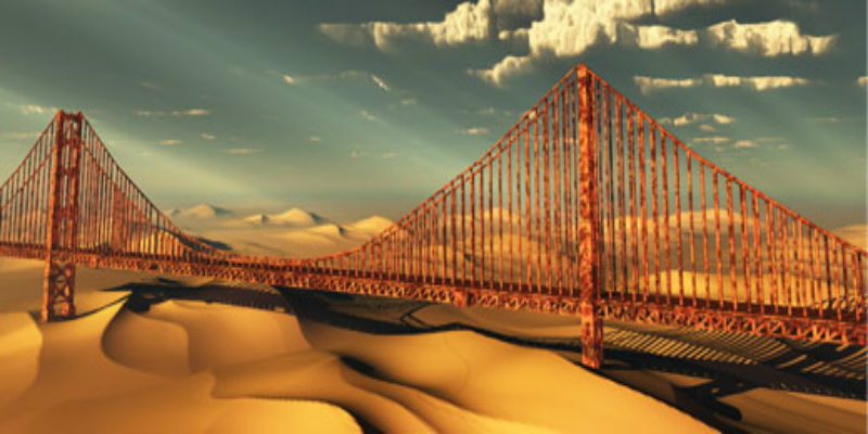 A rusty bridge against a background of sand dunes and a darkening, cloud-filled sky.