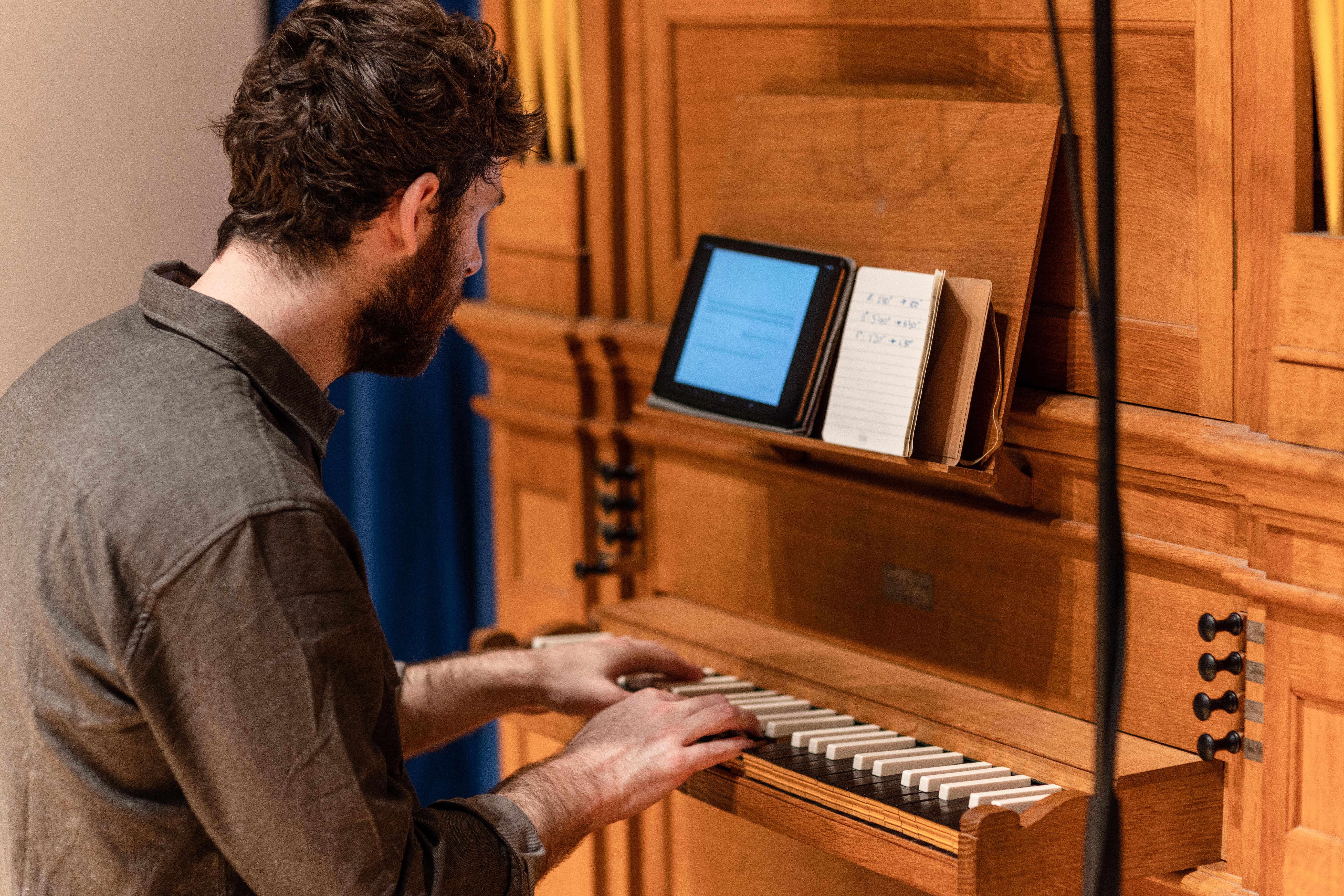 Student practicing on the chamber organ in the Clothworkers Centenary Concert Hall, the image is taken from an angle to the side and they are looking at a screen as they play.