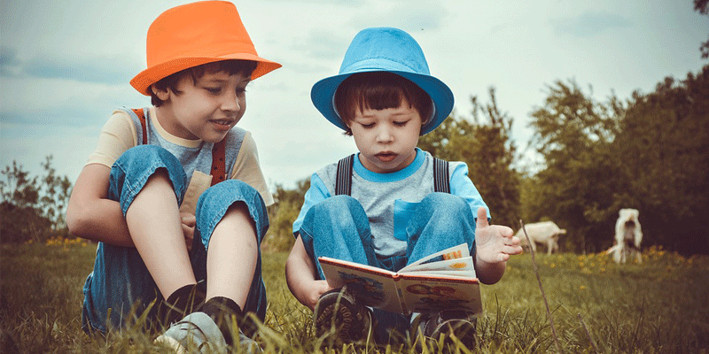 Image of two young boys sat on the grass wearing hats