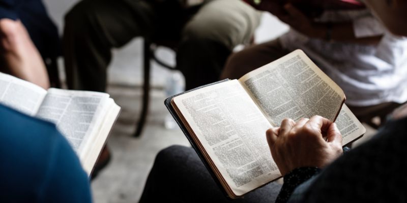 close up of a circle of people facing inwards reading bibles.