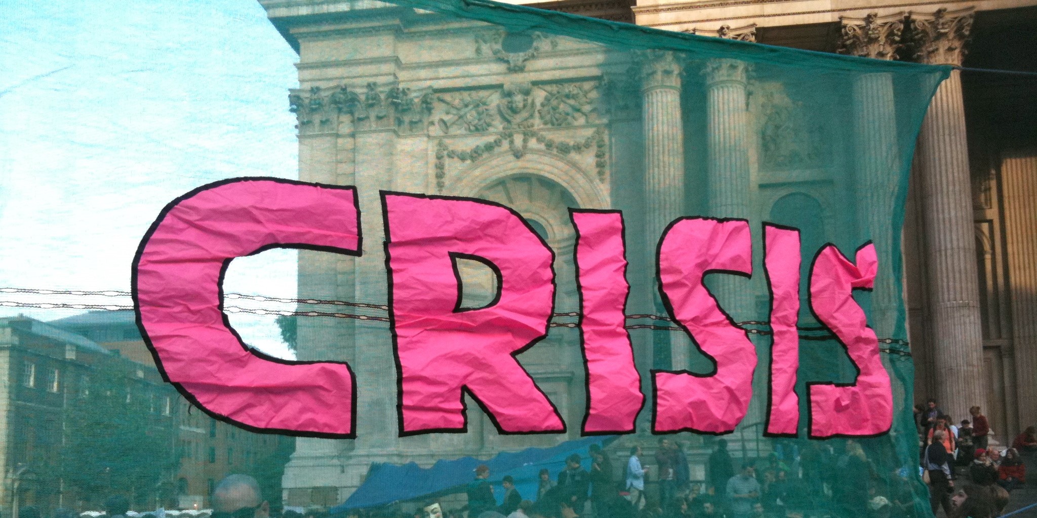 A green banner with "CRISIS" sewn on it in bold pink letters.