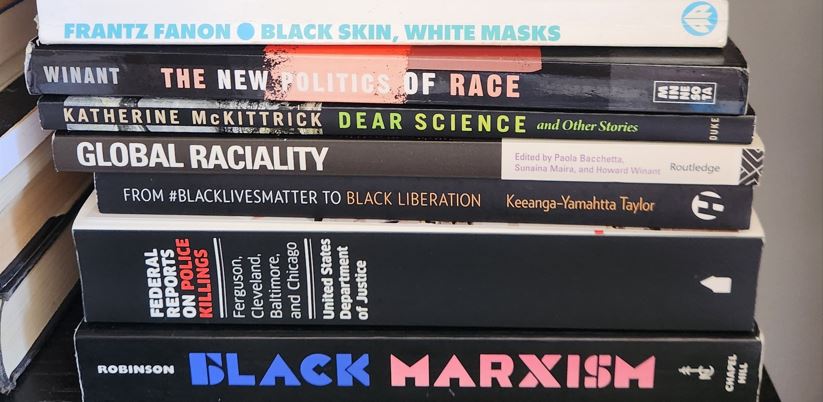 A pile of books about race including "Black Skin, White Masks," "Global Raciality," and "Black Marxism."