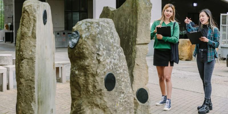 Stone sculptures by Lorna Green situated on the University of Leeds campus, with two onlookers