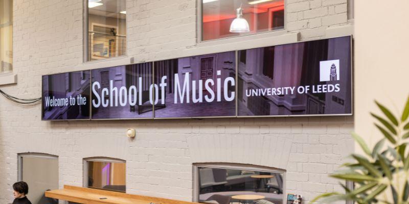 Three screens in the School of Music attached to the wall reading &#039;Welcome to the School of Music, University of Leeds&#039;.