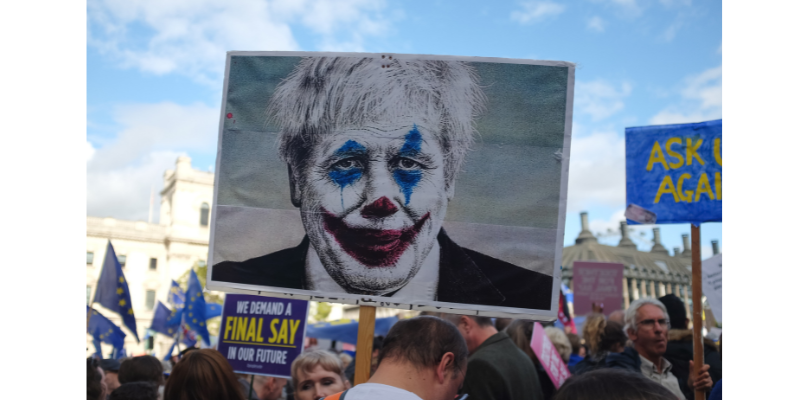 Political protest; protester holding sign with depiction of Boris Johnson in clown makeup