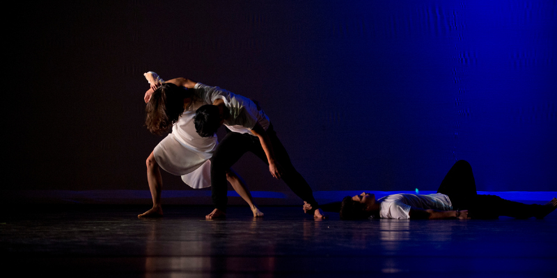 Still image of a dancer performance, three dancers on a dark black background