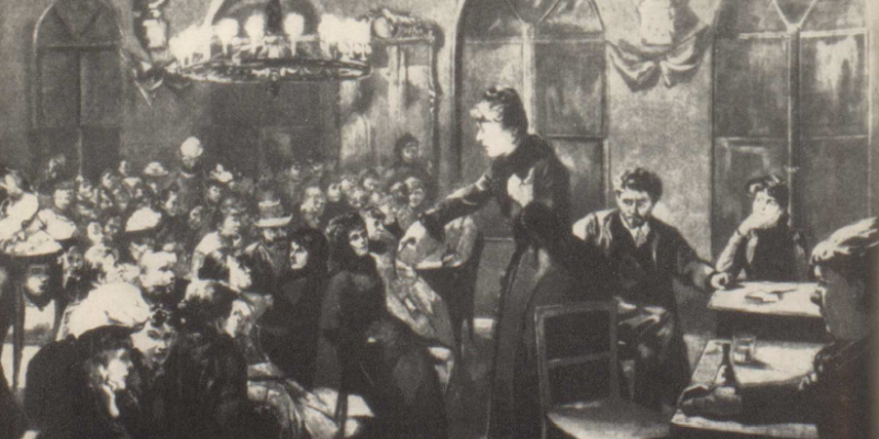 It is an impression of a (illegal/semi-legal) meeting of German socialist women in 1891 in Berlin. A woman stands at the front of a room in front of a crowd of people sat at tables.