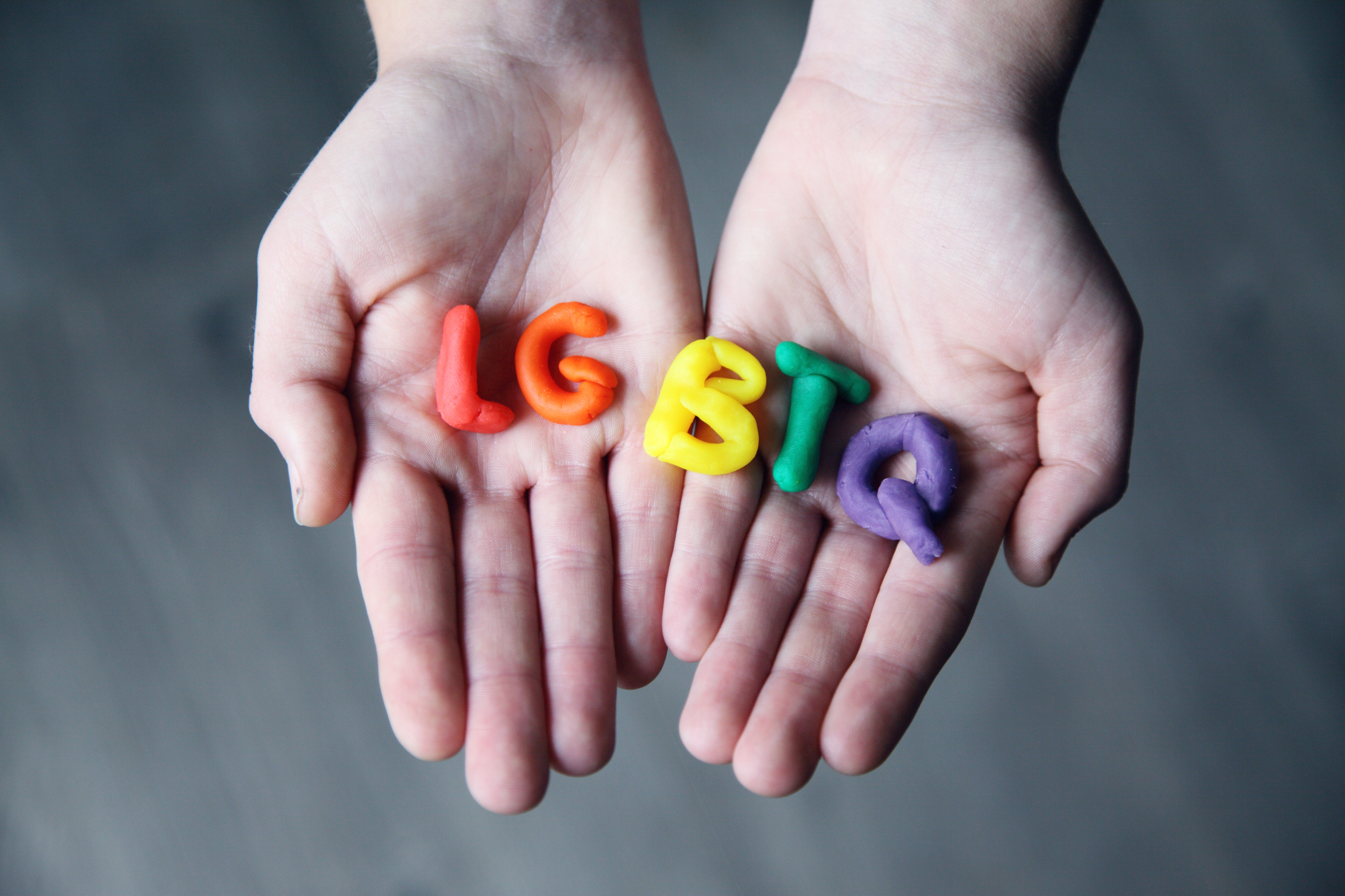 Hands holding colourful letters spelling LGBTQ