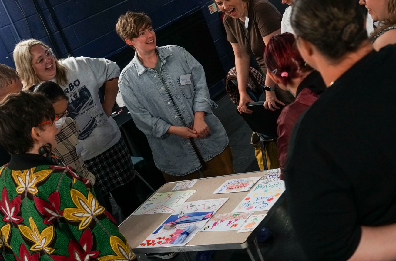 A smiling group of people. They are standing around a table with posters on it