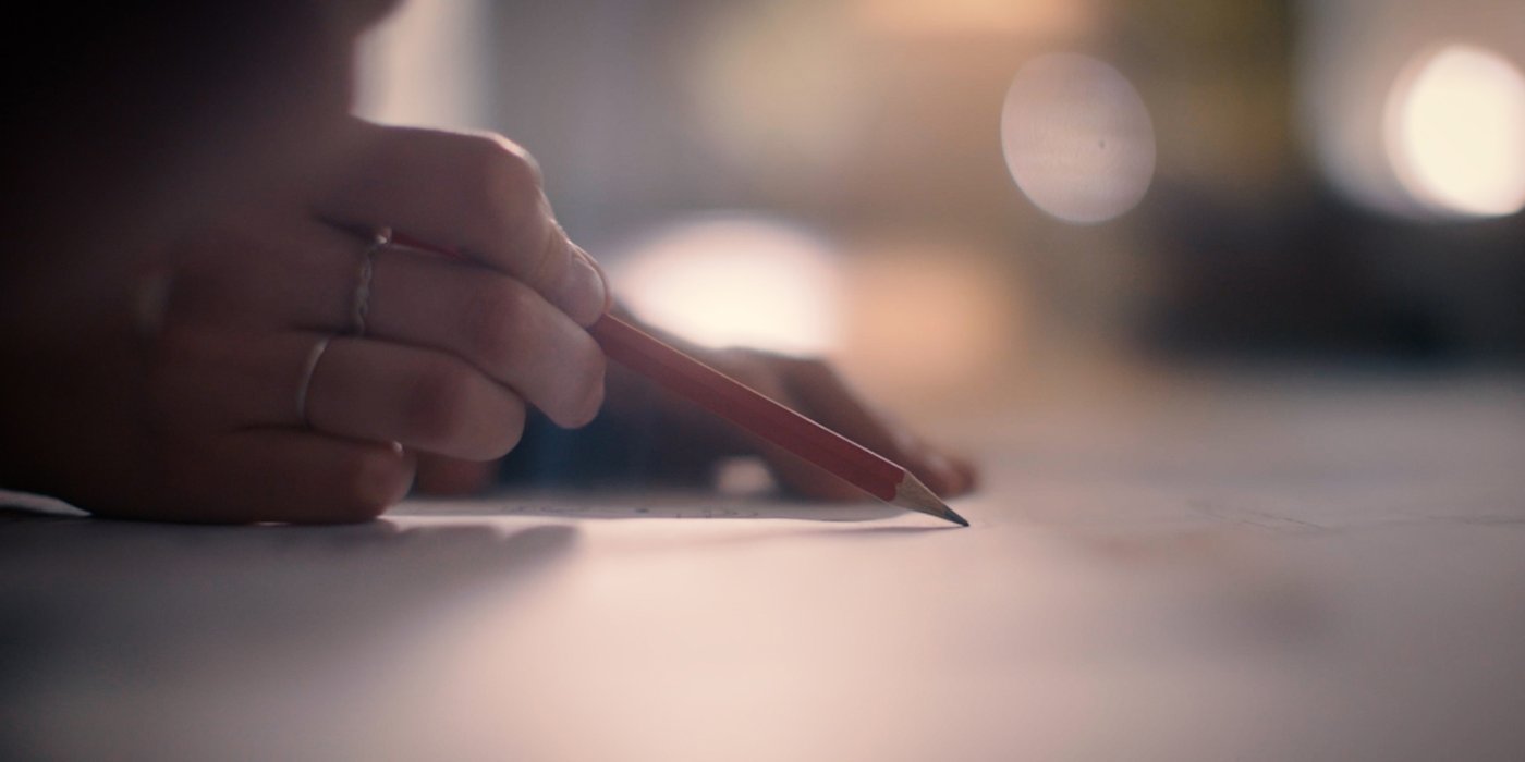 A photo of a hand holding a pencil and sketching in low light.