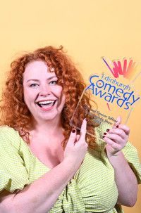 Award winner smiling, stood against yellow backdrop, holding award, wearing a green top