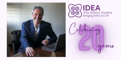 Gavin Esler sat at a desk to the left, IDEA logo and the words celebrating 20 years to the right