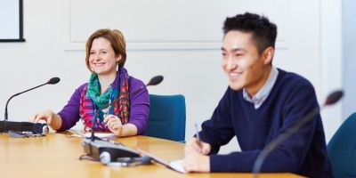 Two smiling people sat around a large circular table in a meeting setting