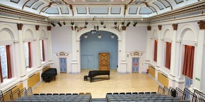 Interior of a  concert hall with a grand piano at the front.