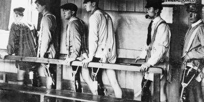 Black and white photograph showing men with amputations walking by using a handrail for support.