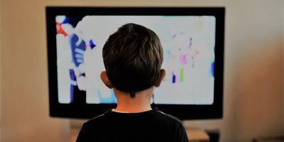 A boy with his back to the camera, watching television
