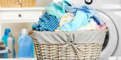 A short wicker clothes basket full of clothes on a table in front of a washing machine.