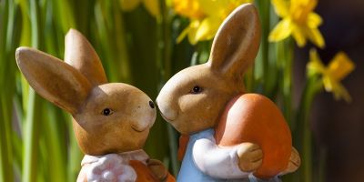 Two ornamental bunny rabbits standing in daffodils, holding easter egg.