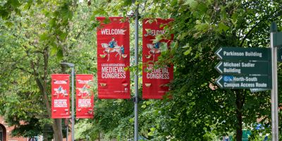 Red banners advertising the International Medieval Congress seen through trees on the University of Leeds campus