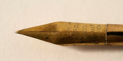 A brass fountain pen nib against a beige paper background