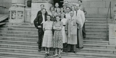 Black and white photo of a group of people standing on steps to a building