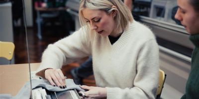 Women demonstrating with fabric on a knitting machine