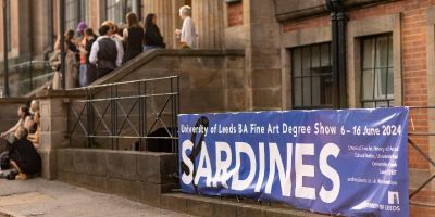 Building with people on the steps and a banner to the foreground advertising the Sardines BA Fine Art Degree Show at the University of Leeds