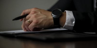 Arm in a suit sleeve and watch resting on desk with a pen