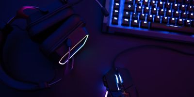 A computer keyboard, mouse and headphones with neon backlights.