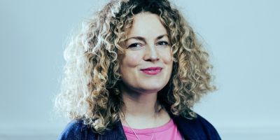 Headshot of Evie Manning. Evie has blond curly hair, wearing a pink top and blue jacket.