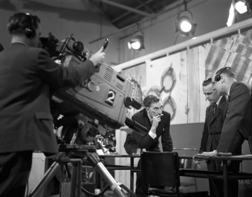 Black and white image of men in suits in a TV recording studio