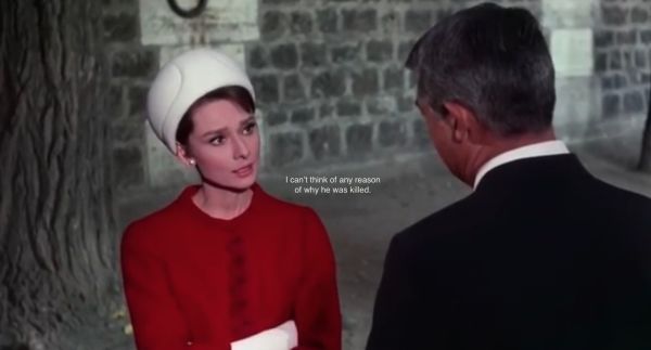 A screenshot from a film showing a woman in red and a man in a black suit, with subtitles on the front of the image