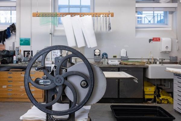 Printmaking workshop in the School of Fine Art, History of Art and Cultural Studies. Featured is a printing press, prints drying on an elevated rack and other printing equipment on cabinets in the background.